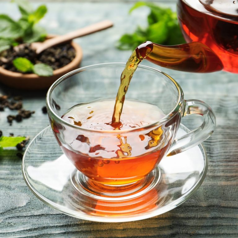 Pouring black tea into glass cup on wooden table